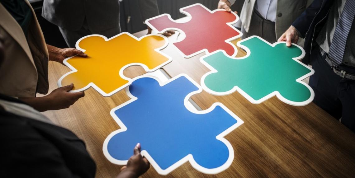 Hands of business people around a table each holding a puzzle piece