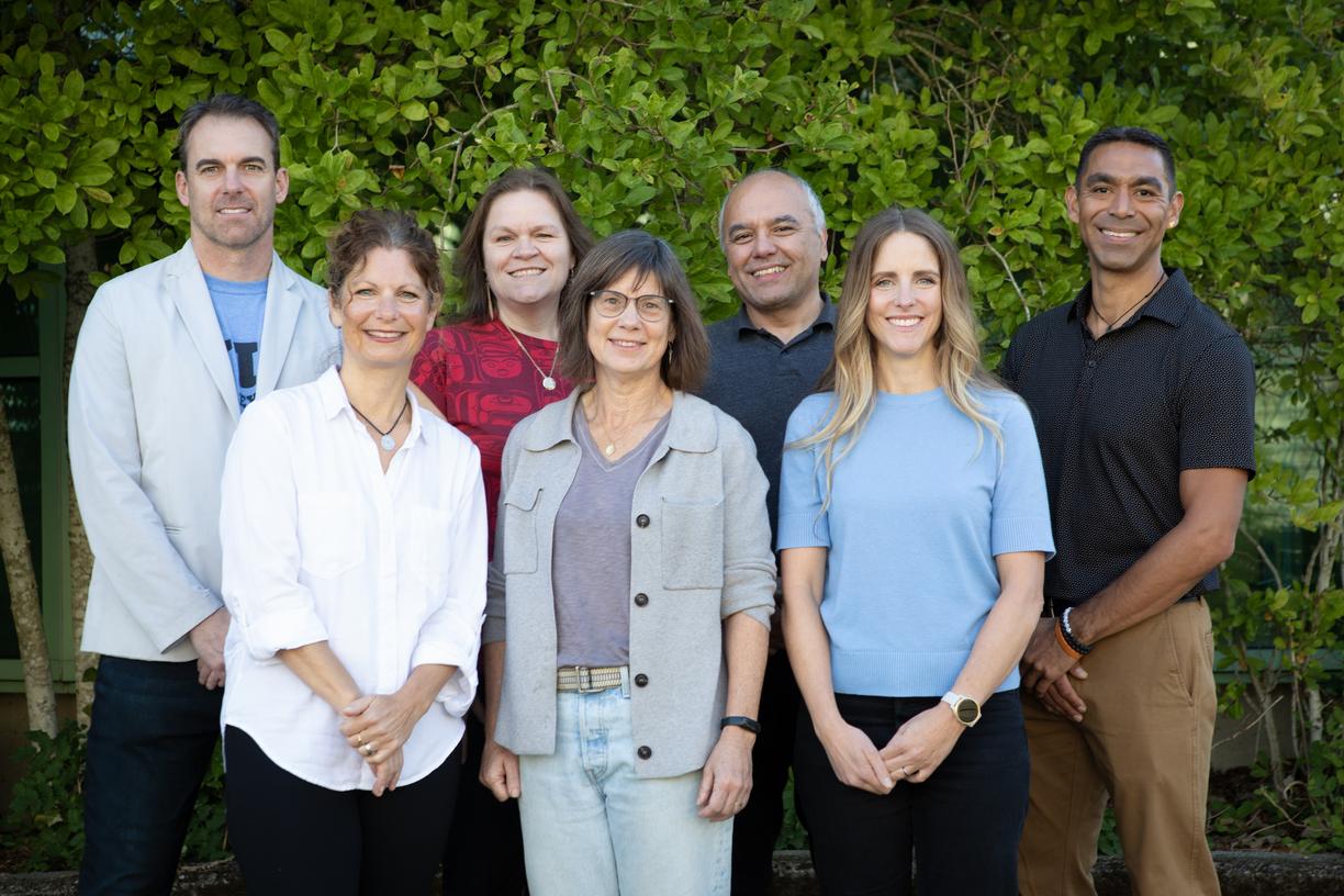 Smiling men and women standing together in front of bushes