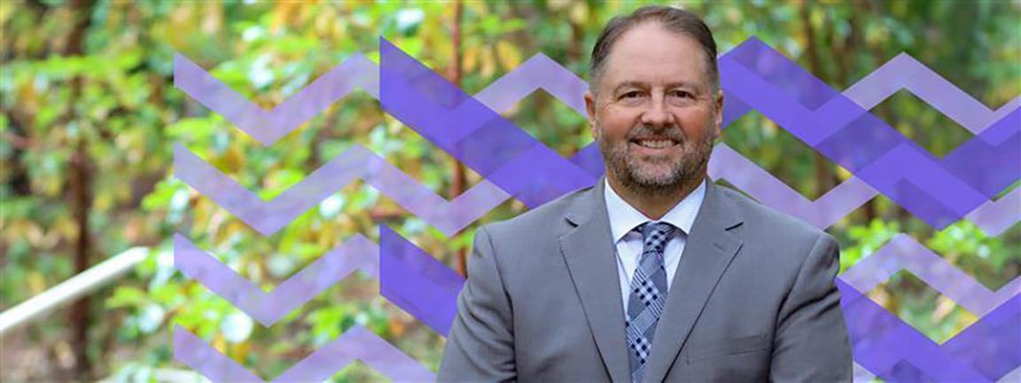 Dennis Johnson with trees in the background and overlaid with the VIU waves graphic