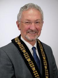 A smiling man wearing a mayoral sash and a suit.