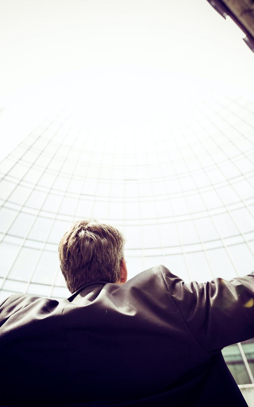A business man preading his arms and looking upwards towards skyscrapers